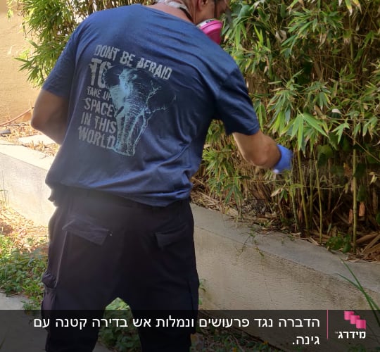 אדם עם מסכת מגן מרסס חומר הדברה בגינה
